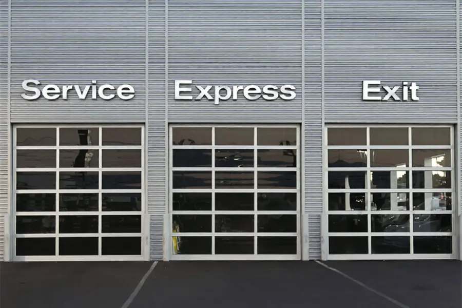 Triple full-view glass commercial sectional doors installed at a professional automotive service center.