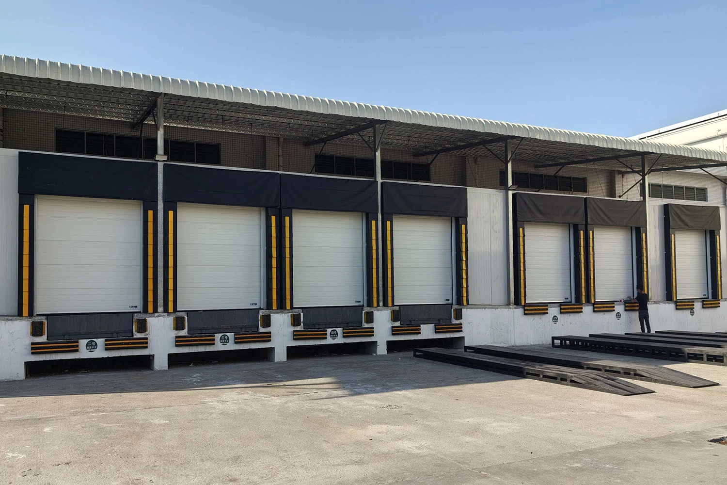 Exterior view of a modern logistics center featuring a row of commercial dock high doors integrated with heavy-duty dock seals and levelers. ABX OEM manufacturer provides CE/ISO certified loading bay integration solutions for global wholesale projects.