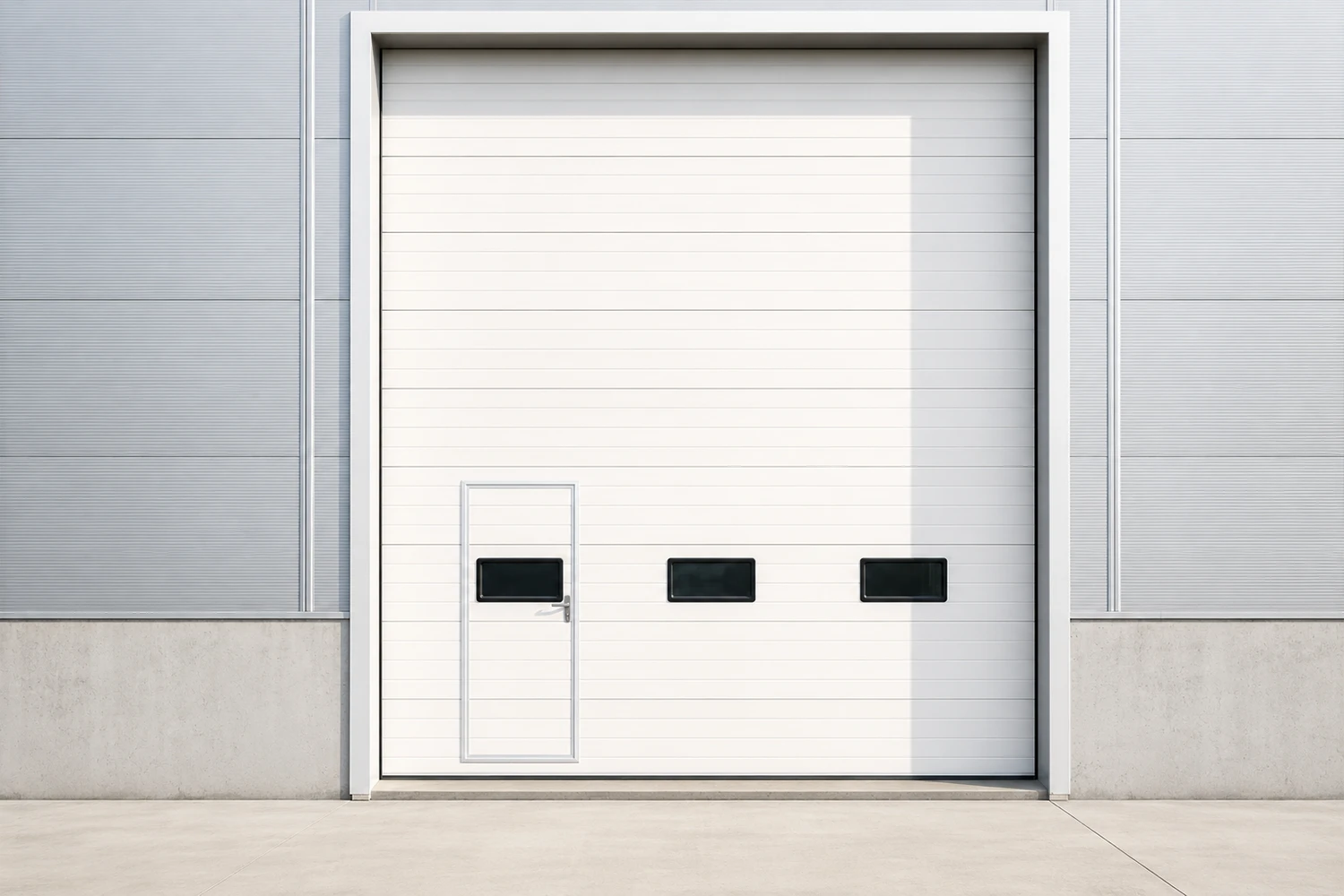 White custom commercial sectional door featuring an integrated wicket door for pedestrian access and rectangular vision windows, installed on a modern factory facade.