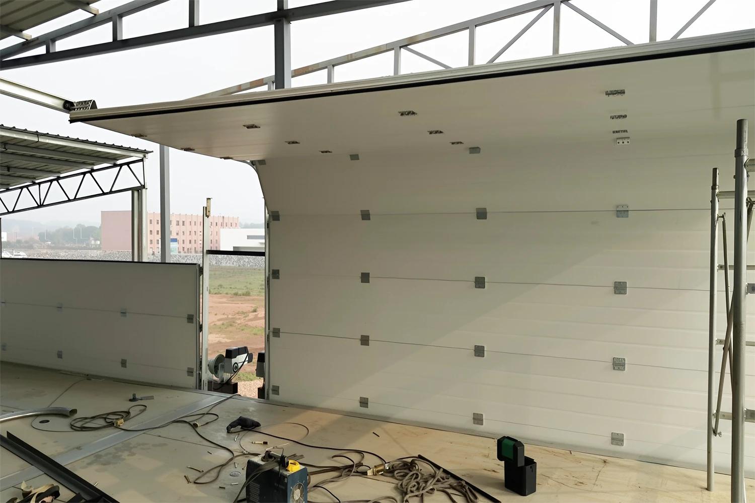 On-site installation process of an ABX heavy-duty commercial overhead door in an industrial facility, following strict manual tolerances to maximize MTBF and operational uptime.
