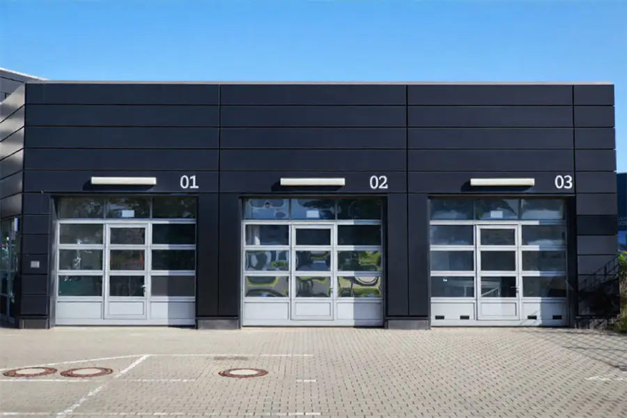 Row of modern grey full-view aluminum sectional doors with clear glass panels for industrial buildings.