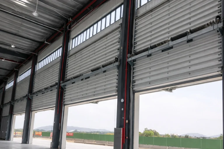 Interior view of oversized industrial sectional doors equipped with heavy-duty torsion springs and vision panels, engineered for high wind load resistance in a heavy manufacturing facility.